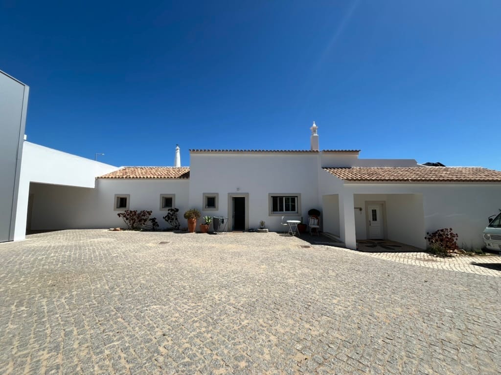Single-storey whitewashed farmhouse with a terracotta pantile roof behind a cobbled forecourt