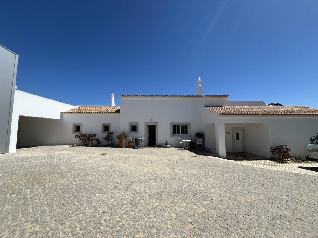 Single-storey whitewashed farmhouse with a terracotta pantile roof behind a cobbled forecourt